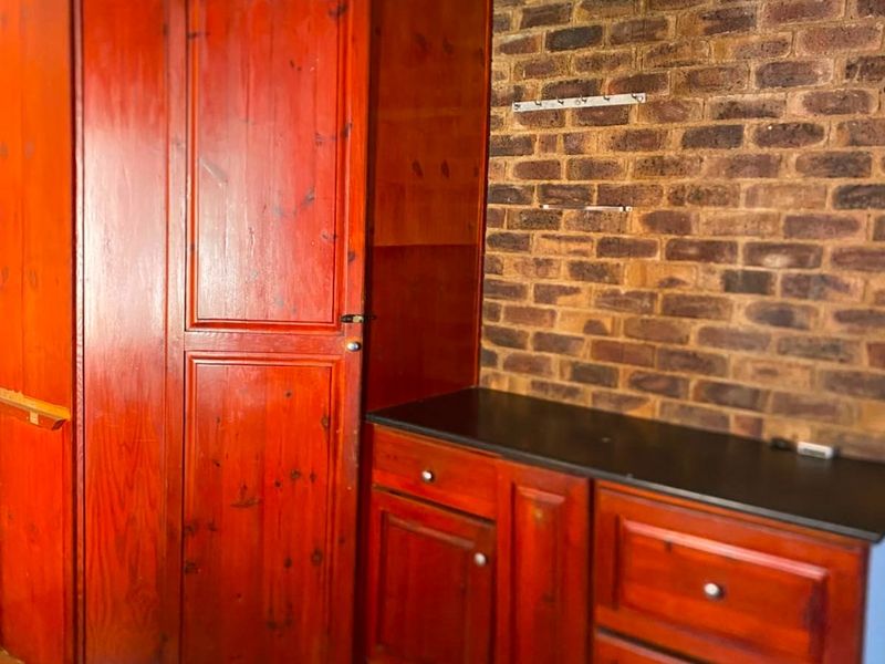 A utility space featuring built-in wooden cabinetry, an exposed brick feature wall, and tiled flooring, offering functional storage potential.