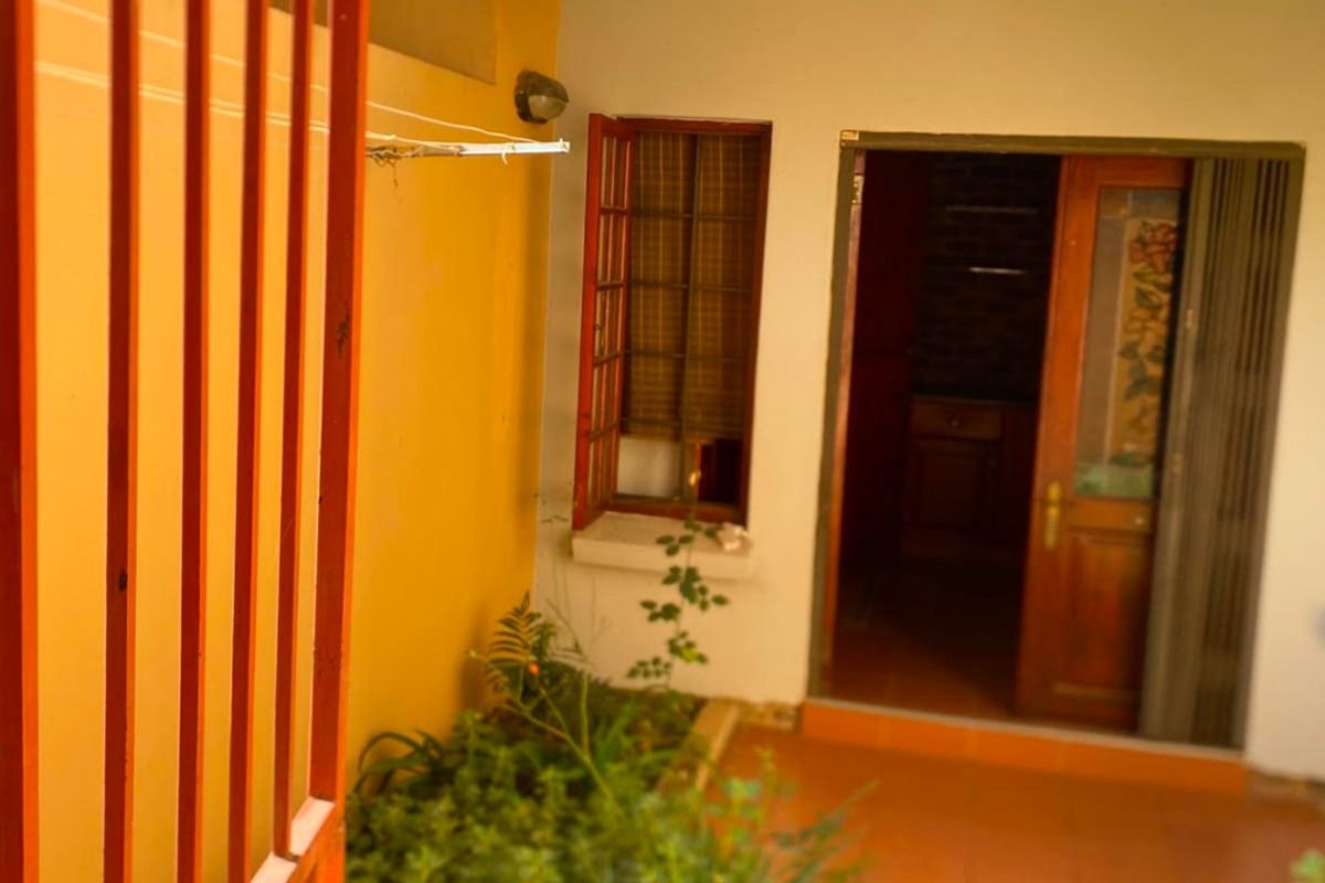 A rear exterior view showing a paved courtyard area, a tiled roof overhang, and access to the interior through a timber door.