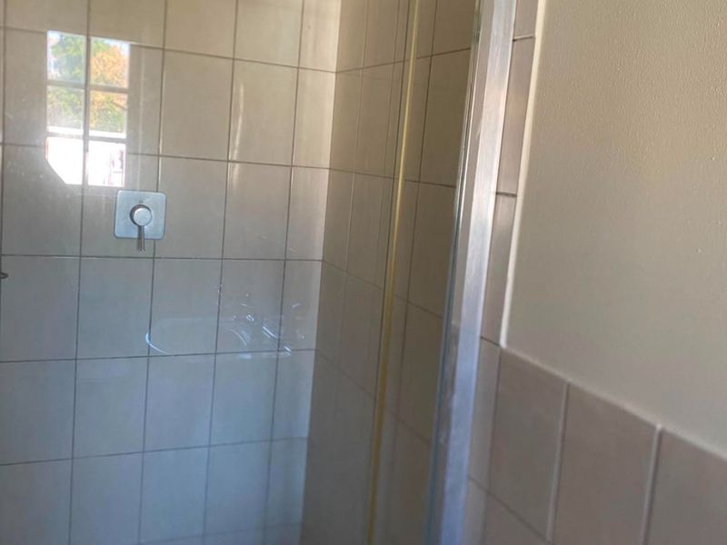 A functional bathroom shower enclosure featuring tiled walls, a mosaic-style tiled floor, and a modern chrome mixer tap.