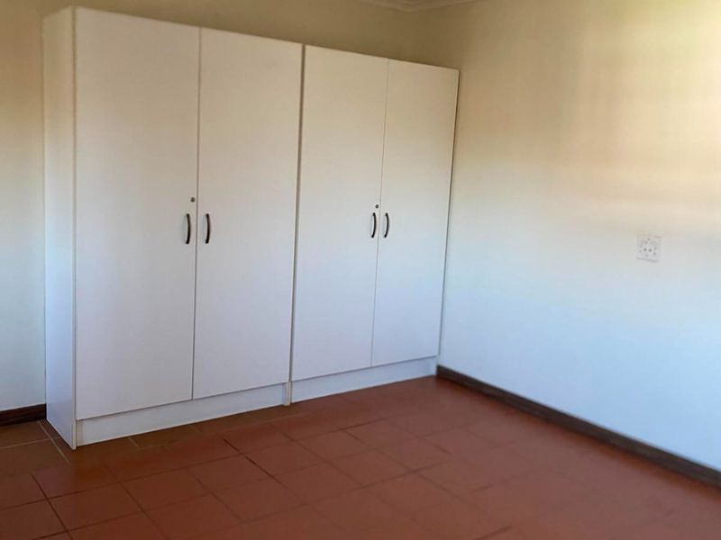 A simple, empty bedroom featuring built-in white cupboards and terracotta-style tiled flooring, offering a clean canvas for personalization.