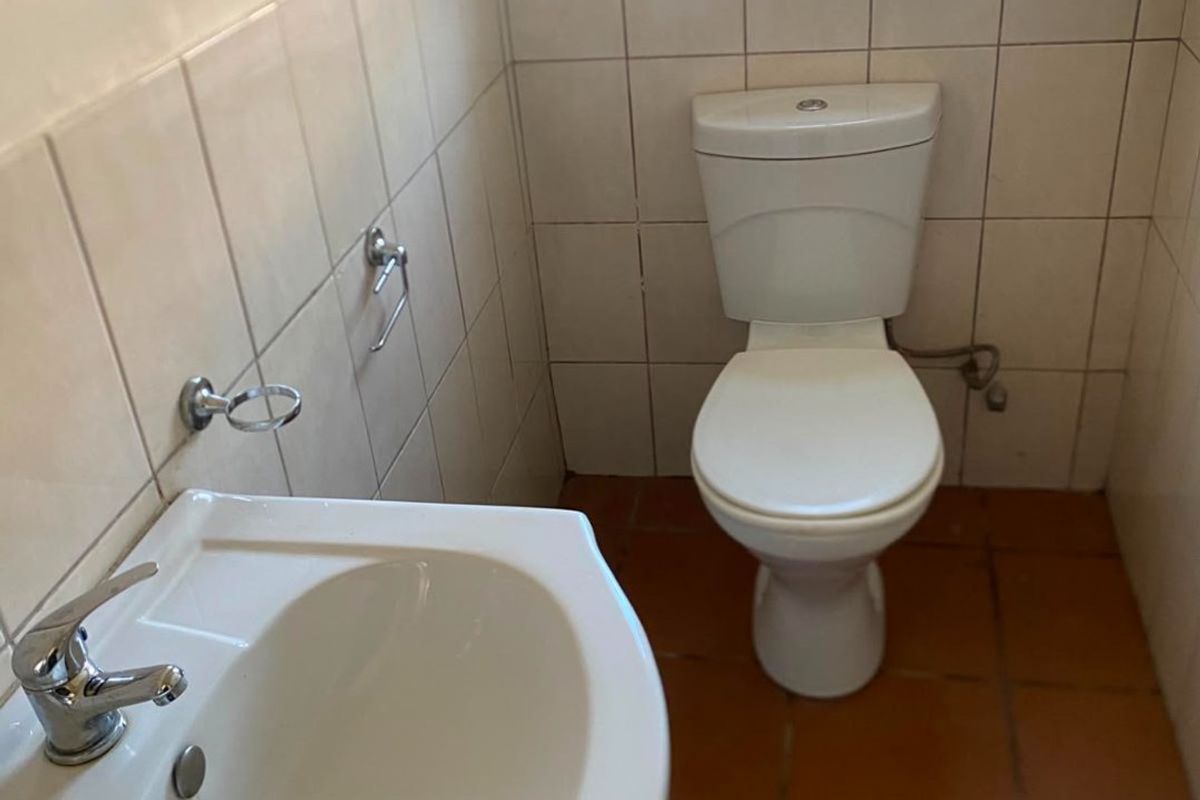 A functional guest bathroom featuring a pedestal basin, chrome mixer tap, ceramic toilet, and neutral wall tiling.