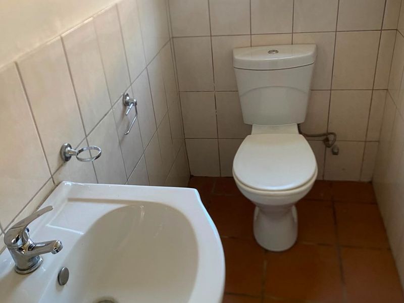 A functional guest bathroom featuring a pedestal basin, chrome mixer tap, ceramic toilet, and neutral wall tiling.