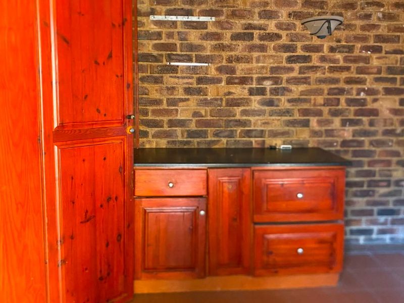 A functional scullery or utility area featuring built-in wooden cabinetry, a stone countertop, and an exposed brick feature wall with tiled flooring.