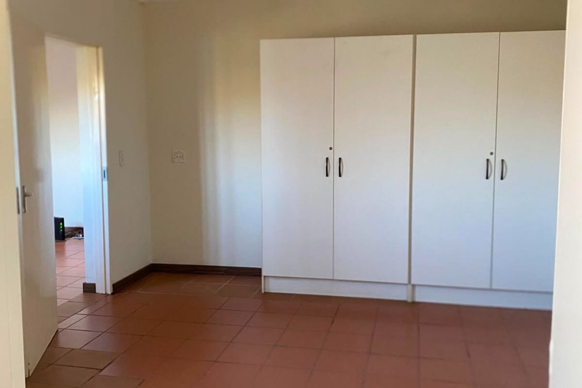 A spacious, empty bedroom featuring built-in cupboards and terracotta-style tiled flooring, offering a blank canvas for personalization.