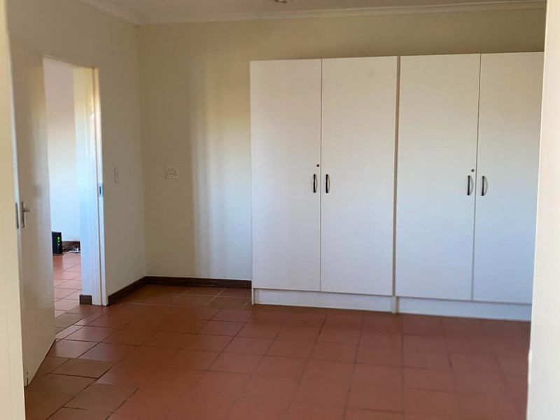 A spacious, empty bedroom featuring built-in cupboards and terracotta-style tiled flooring, offering a blank canvas for personalization.