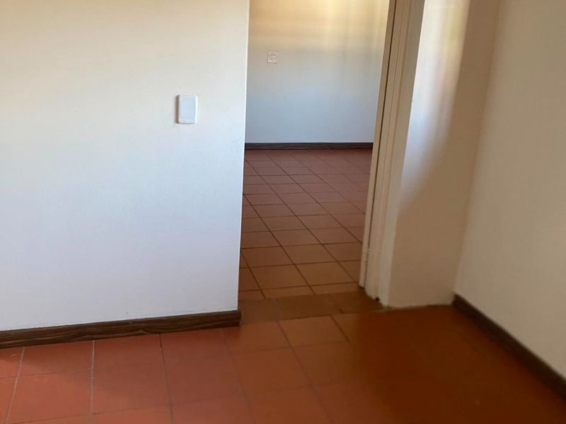 A simple interior hallway featuring terracotta floor tiles and timber skirting boards, connecting two vacant rooms.