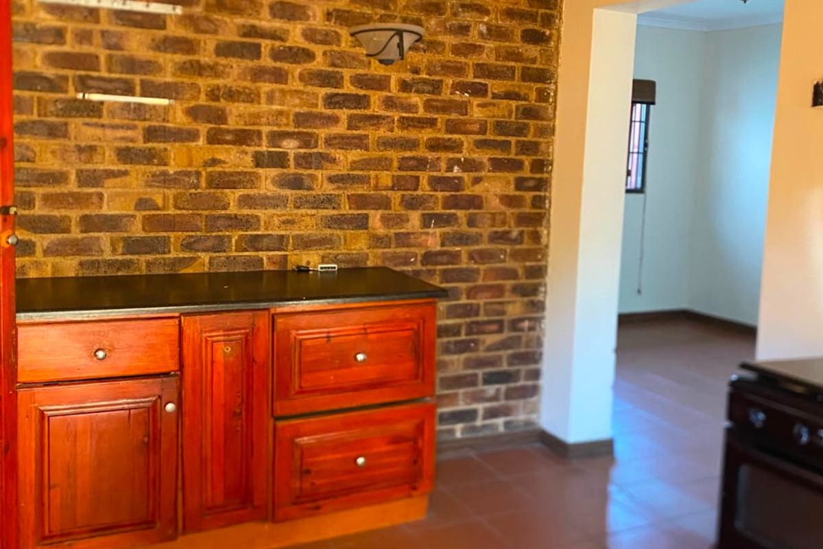 Kitchen area featuring an exposed brick feature wall, built-in wooden cabinetry with stone countertops, and ceramic tile flooring.