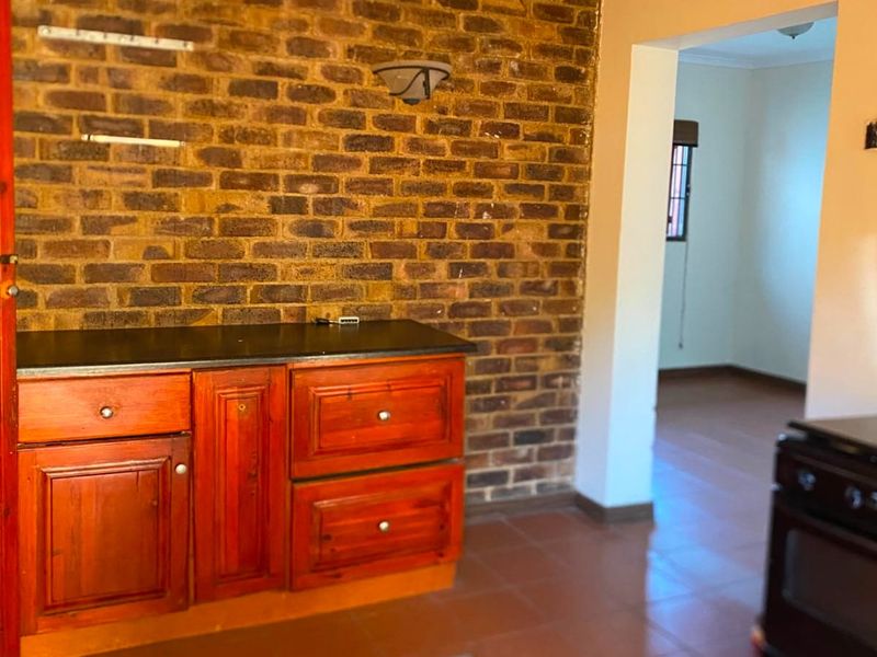 Kitchen area featuring an exposed brick feature wall, built-in wooden cabinetry with stone countertops, and ceramic tile flooring.