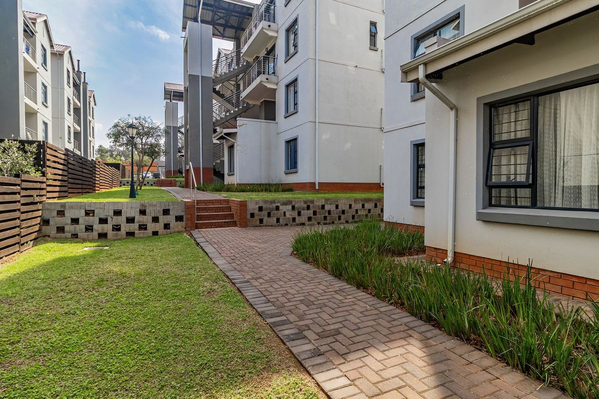 A well-maintained exterior view of the apartment complex featuring paved walkways, landscaped garden areas, and modern building architecture.