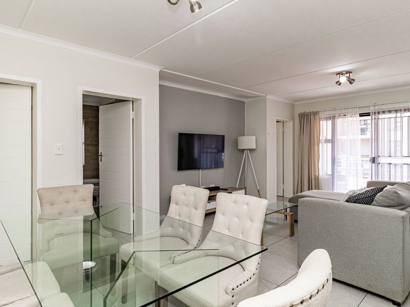 A bright open-plan living and dining area featuring neutral tiled flooring, modern cove cornicing, and a sliding glass door leading to an outdoor space.