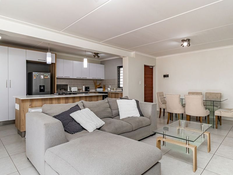 Modern open-plan living area featuring a contemporary kitchen with island, sleek cabinetry, and tiled flooring, seamlessly flowing into the dining and lounge space.