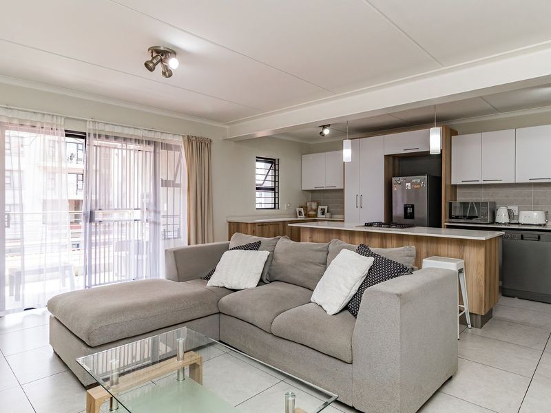 Modern open-plan living area featuring a contemporary kitchen with island, tiled floors, and direct access to a balcony through sliding glass doors.