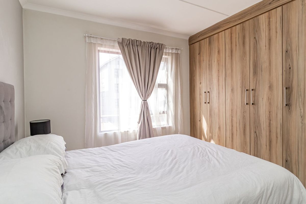 A well-maintained bedroom featuring extensive floor-to-ceiling built-in wooden cupboards and natural light from a window.