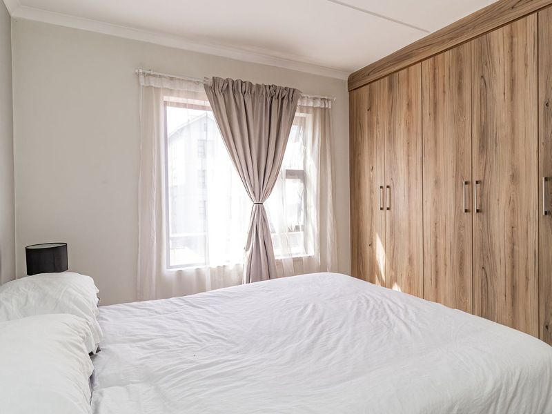 A well-maintained bedroom featuring extensive floor-to-ceiling built-in wooden cupboards and natural light from a window.