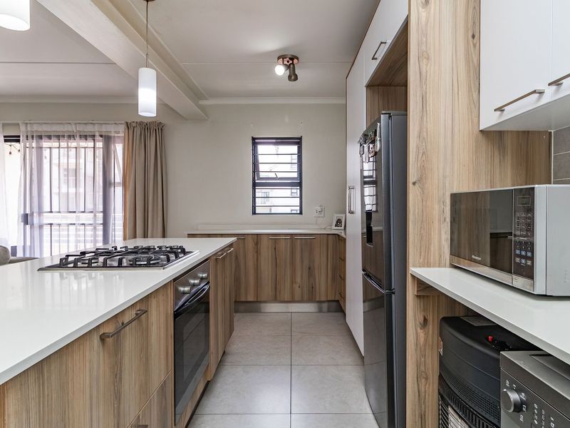 Modern kitchen featuring wood-finish cabinetry, stone countertops, a central island with a gas hob, and tiled flooring in an open-plan layout.