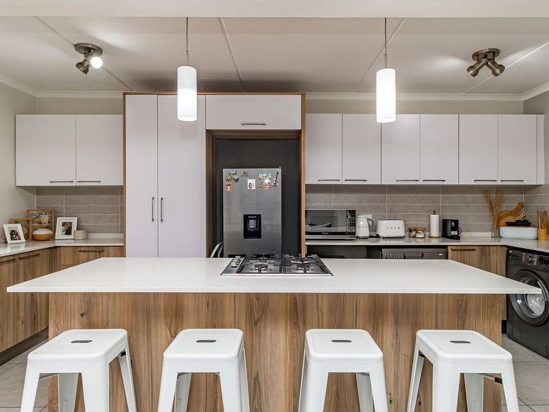 Modern kitchen featuring a central island with a gas cooktop, ample built-in cabinetry, stone countertops, and integrated appliances in a clean, contemporary layout.