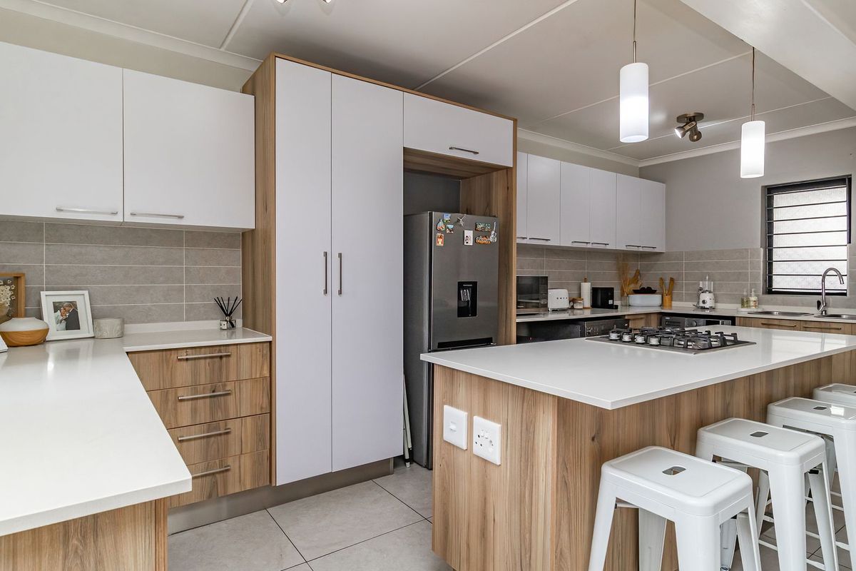 Modern kitchen featuring sleek two-tone cabinetry, stone countertops, a central island with a gas hob, and contemporary tiled finishes.