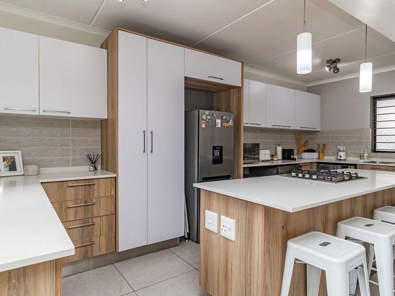 Modern kitchen featuring sleek two-tone cabinetry, stone countertops, a central island with a gas hob, and contemporary tiled finishes.