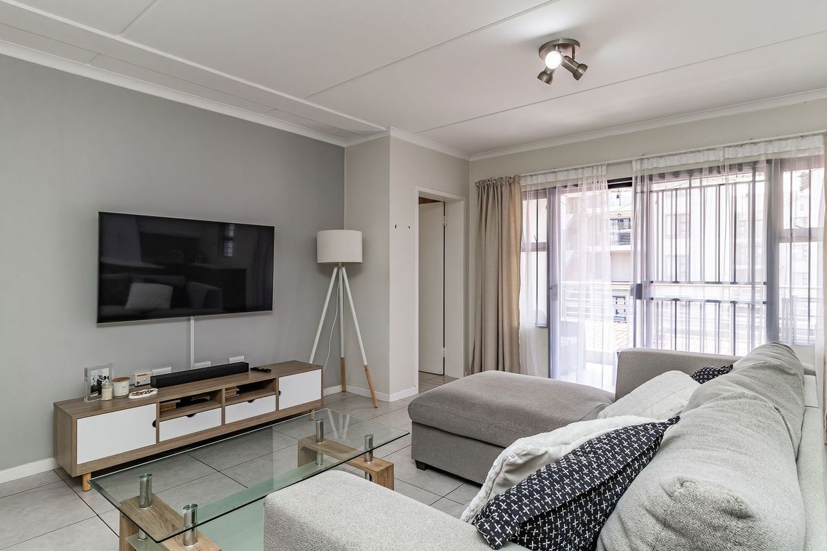 A well-maintained living room featuring neutral grey walls, tiled flooring, and a sliding glass door providing access to an outdoor balcony area.