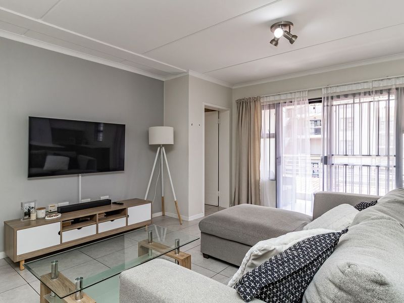 A well-maintained living room featuring neutral grey walls, tiled flooring, and a sliding glass door providing access to an outdoor balcony area.