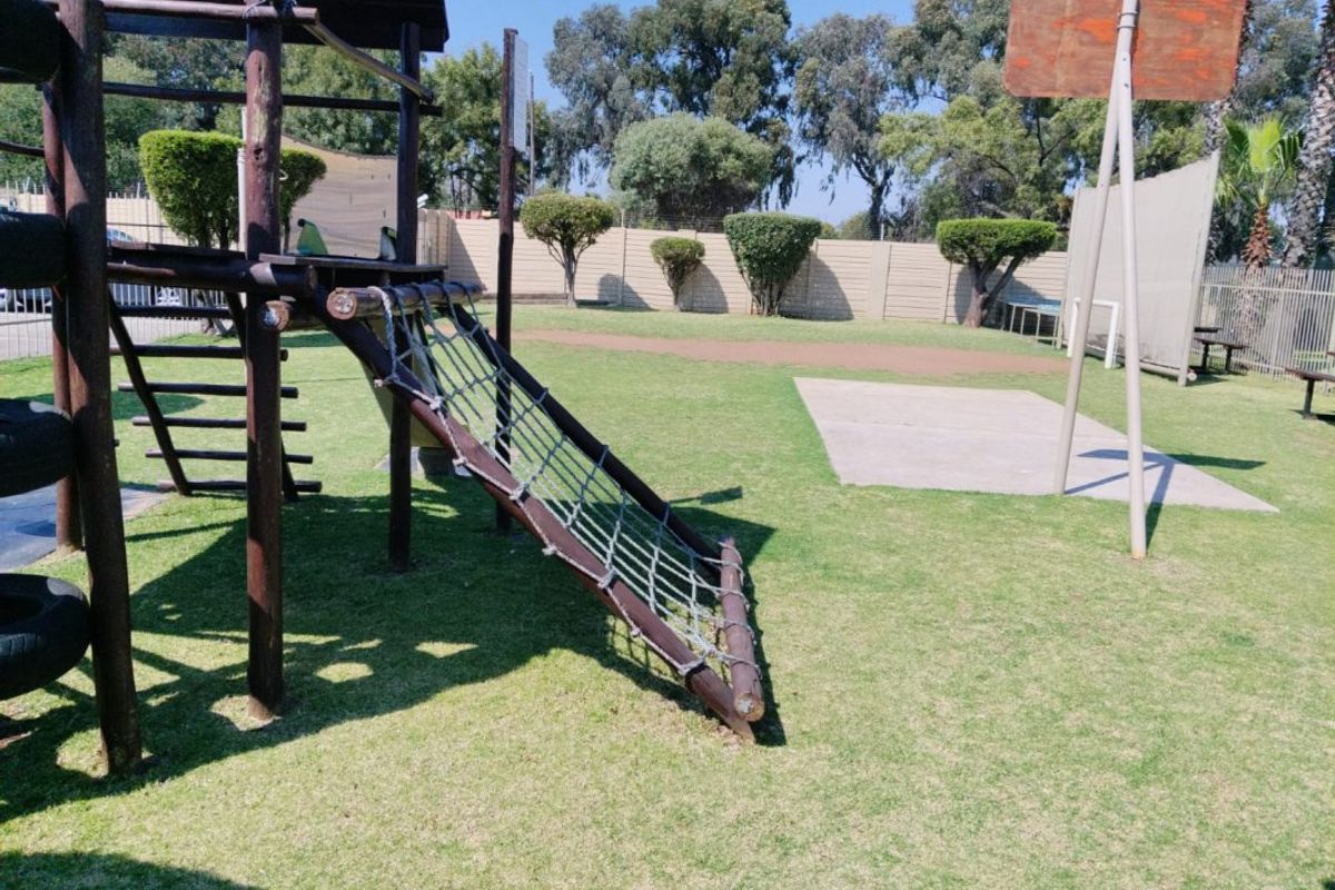 Outdoor communal recreational area featuring a playground structure, basketball hoop, and paved activity space within a fenced complex.