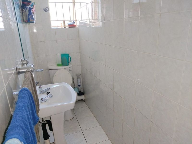 A functional bathroom featuring a pedestal washbasin, toilet, and full-height ceramic wall tiling.