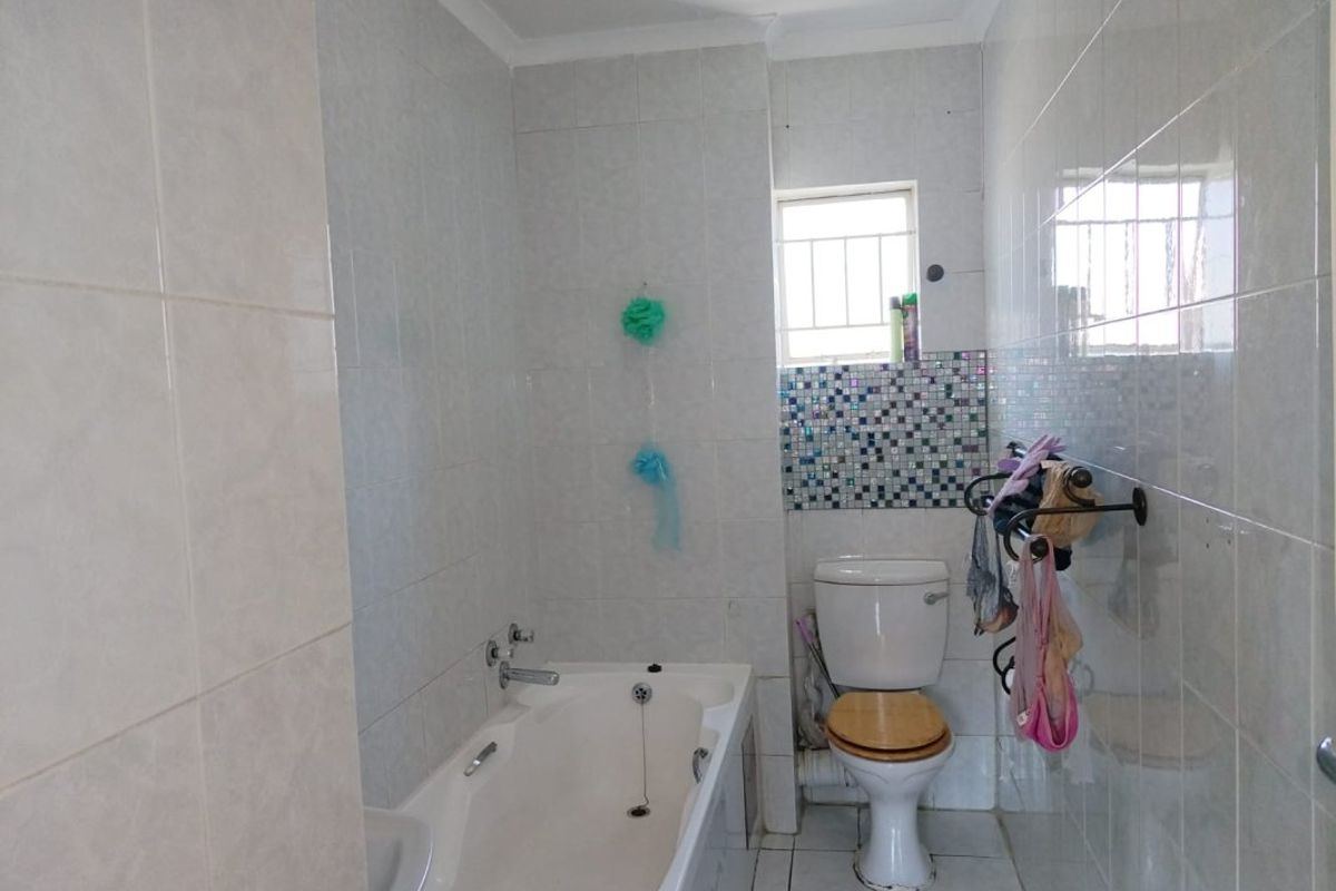 A functional bathroom featuring a bathtub, toilet, and tiled finishes with a mosaic accent wall and a window with security bars.
