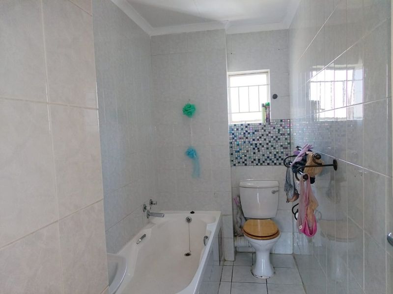 A functional bathroom featuring a bathtub, toilet, and tiled finishes with a mosaic accent wall and a window with security bars.