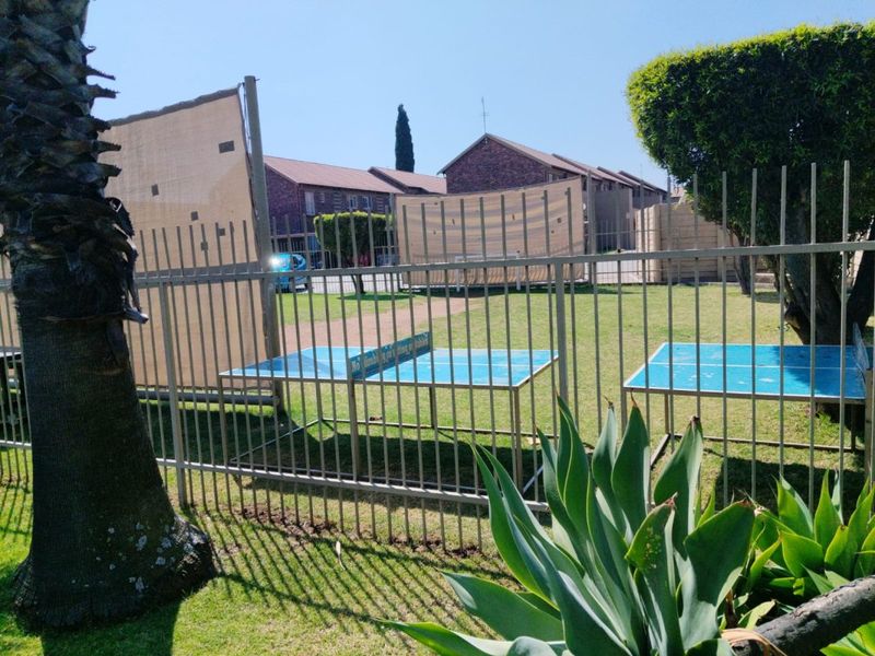 A communal garden area featuring a well-maintained lawn, mature trees, and secure metal perimeter fencing within the apartment complex grounds.