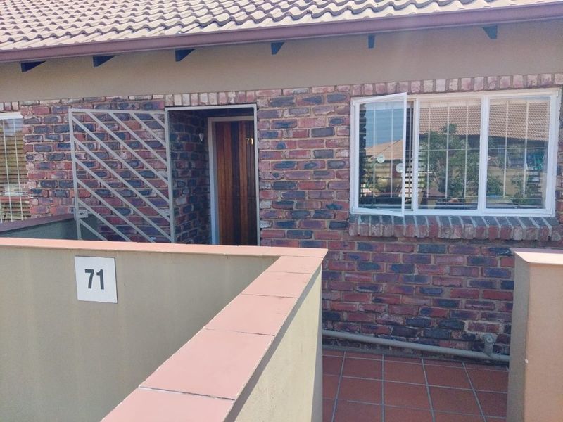 Front entrance view of an apartment featuring a face brick facade, tiled patio, and secure access with a timber door and security gate.
