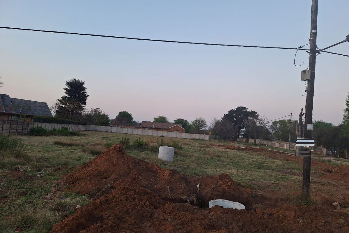 A vacant residential plot featuring a utility pole, precast boundary walling, and recent ground excavation work.