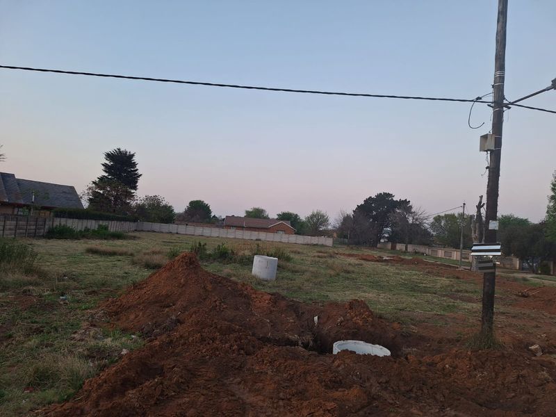A vacant residential plot featuring a utility pole, precast boundary walling, and recent ground excavation work.