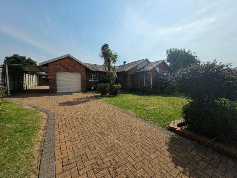 Front view of a brick house featuring a paved driveway, single garage, attached carport, and a well-maintained front lawn.
