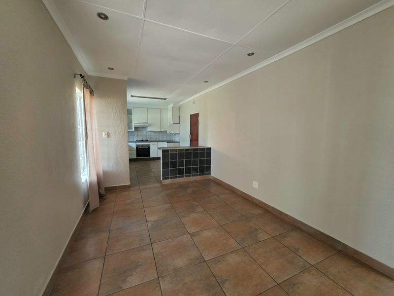 An open-plan living and kitchen area featuring tiled flooring, recessed lighting, and a functional kitchen with built-in cabinetry and appliances.