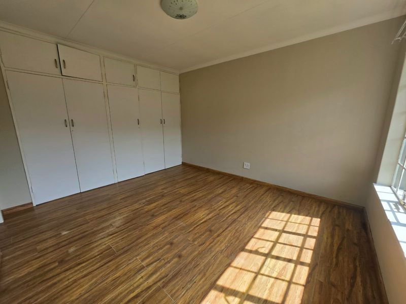 A bright, empty bedroom featuring wood-look laminate flooring and extensive built-in storage cupboards.