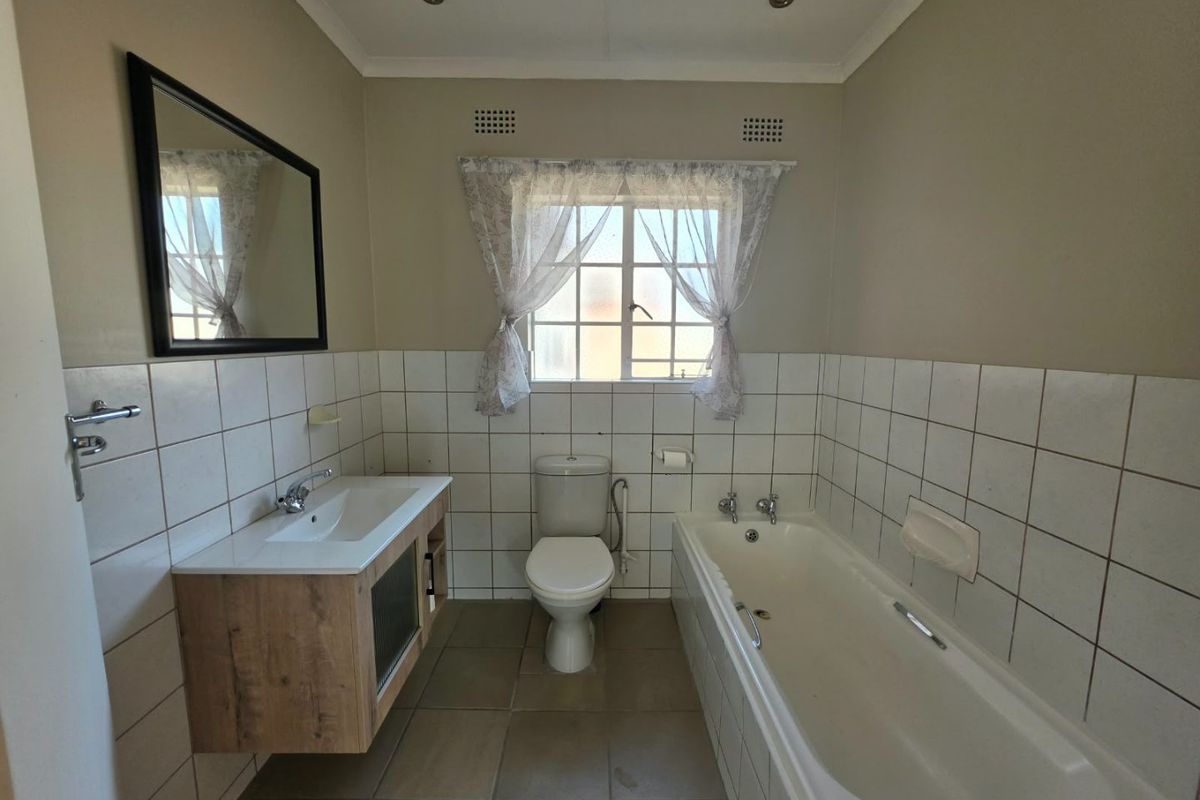A functional bathroom featuring a modern wood-finish vanity, a standard bathtub, and a toilet, with neutral wall and floor tiling throughout.