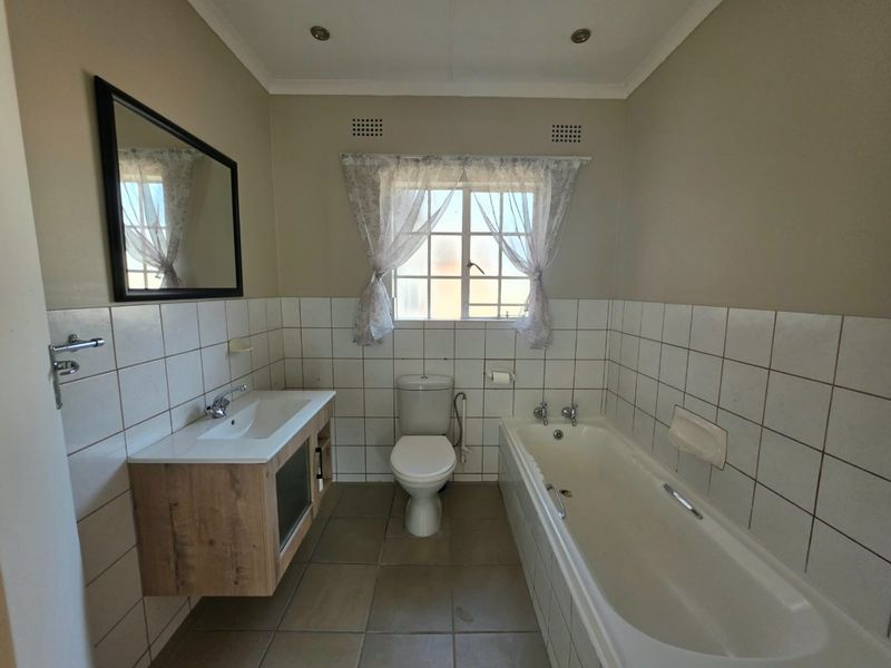 A functional bathroom featuring a modern wood-finish vanity, a standard bathtub, and a toilet, with neutral wall and floor tiling throughout.