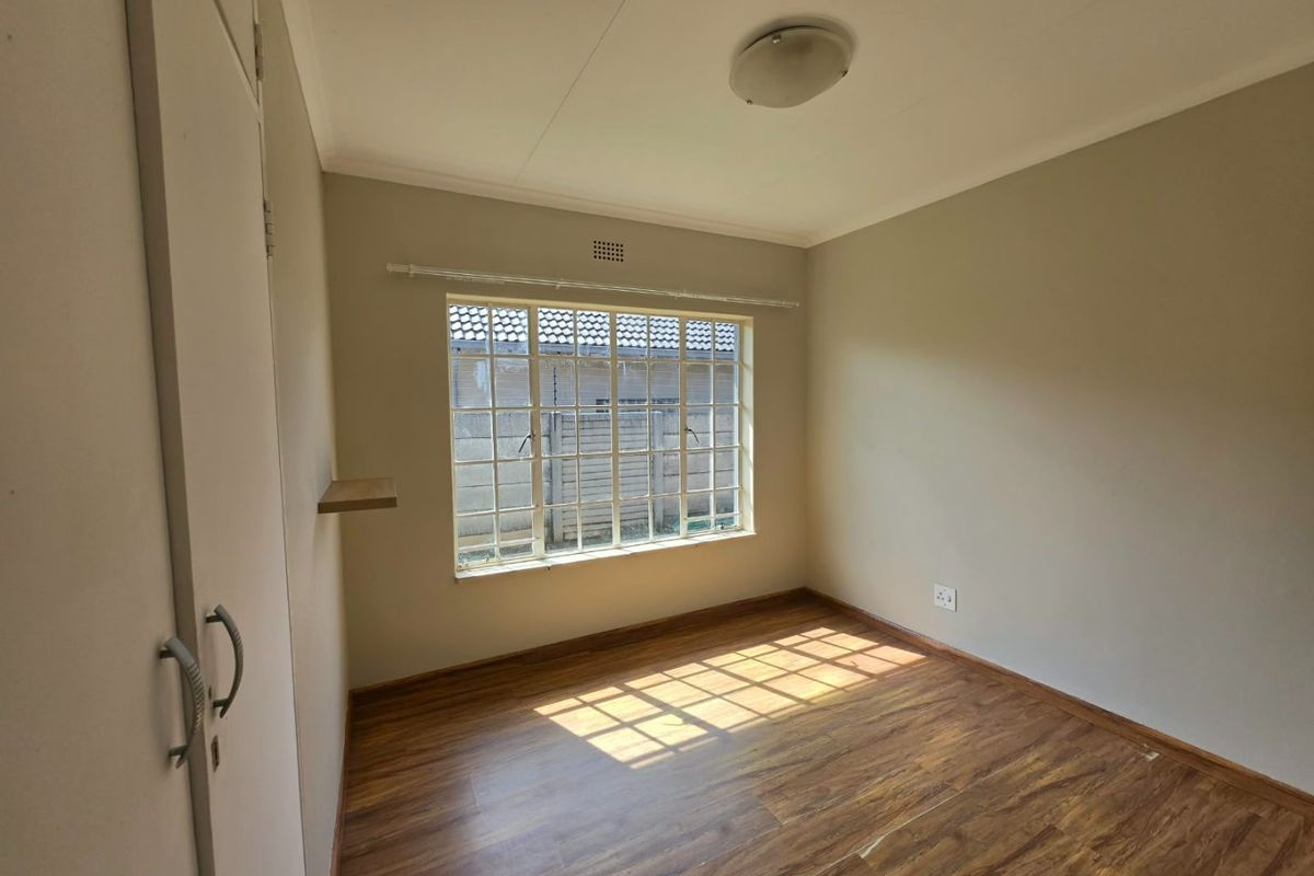 A vacant bedroom featuring laminate flooring, built-in cupboards, and a large steel-framed window providing natural light.