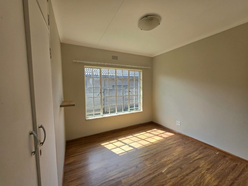 A vacant bedroom featuring laminate flooring, built-in cupboards, and a large steel-framed window providing natural light.