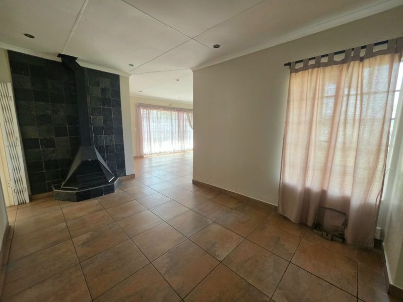 Spacious living area featuring tiled flooring, a prominent tiled fireplace, and recessed ceiling lighting, leading into an adjacent sunlit room.