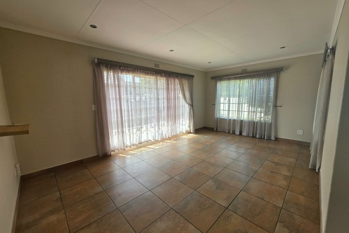 A spacious, empty living room featuring neutral walls, tiled flooring, and large windows with curtain tracks, offering a bright and versatile living space.