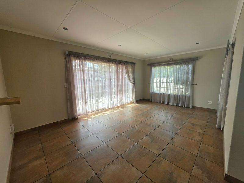 A spacious, empty living room featuring neutral walls, tiled flooring, and large windows with curtain tracks, offering a bright and versatile living space.