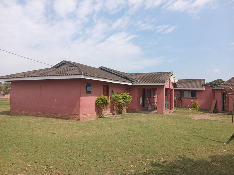 Rear view of a single-story house featuring a tiled roof, brick facade, and a covered patio area set within a spacious garden.