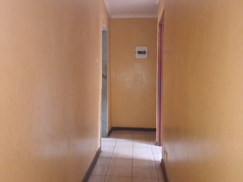A narrow, empty hallway featuring tiled flooring and yellow painted walls, providing access to adjacent rooms within the property.