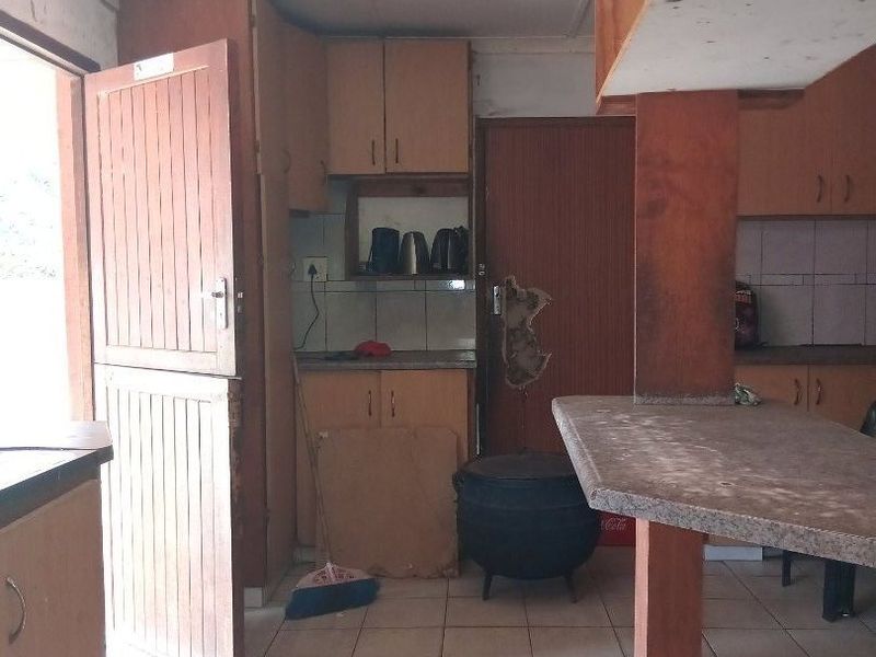 A dated kitchen featuring built-in wooden cabinetry, tiled flooring, and a stable door, requiring significant cosmetic updates and repairs to improve functionality and aesthetic appeal.