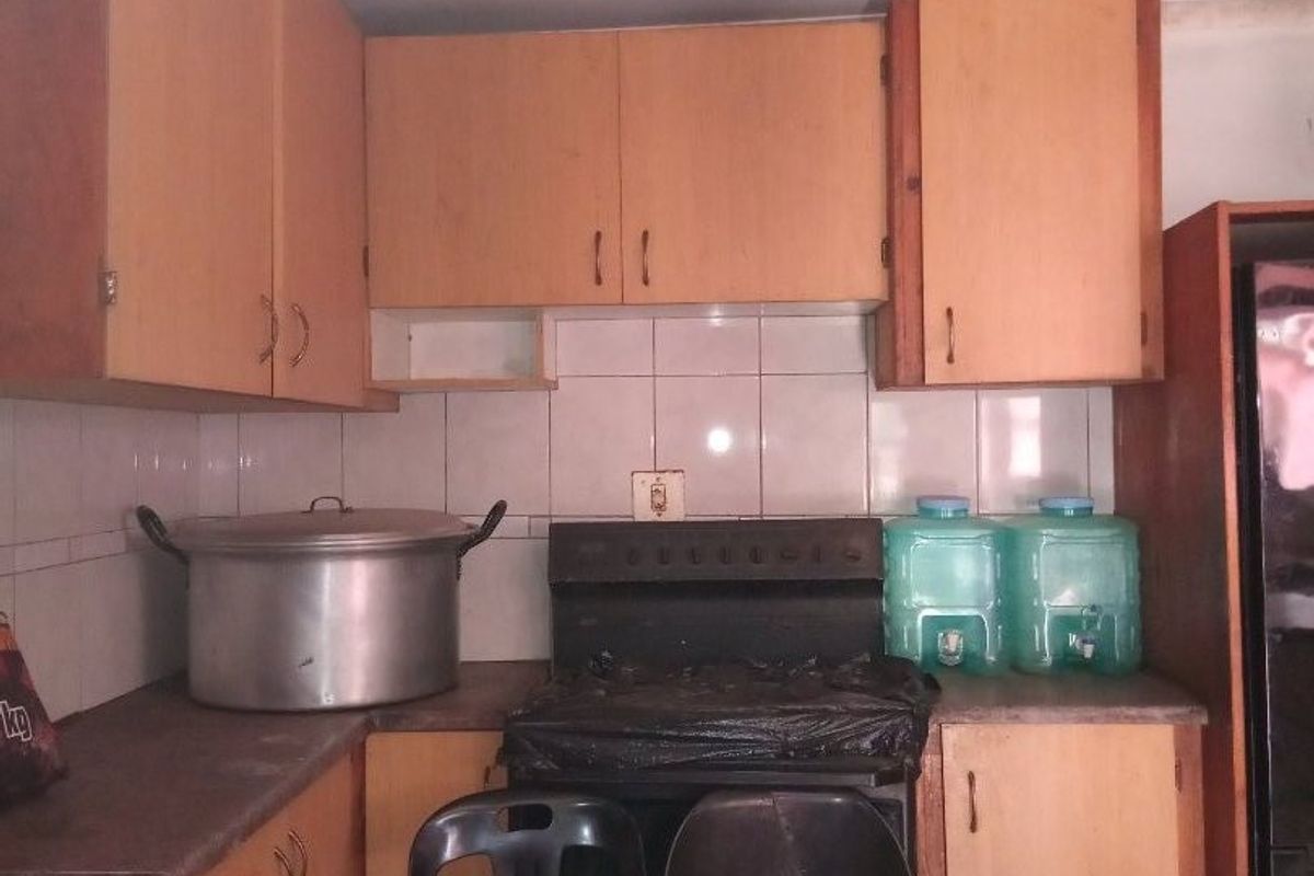 A dated kitchen featuring laminate cabinetry, tiled backsplash, and a freestanding stove, requiring cosmetic updates to improve its overall condition and aesthetic appeal.