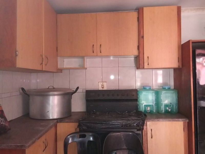A dated kitchen featuring laminate cabinetry, tiled backsplash, and a freestanding stove, requiring cosmetic updates to improve its overall condition and aesthetic appeal.