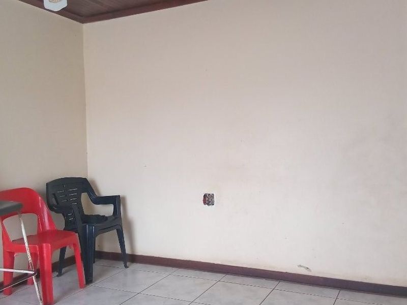 A simple living area featuring tiled flooring, a timber ceiling, and a ceiling fan, currently presenting as a blank canvas for renovation.