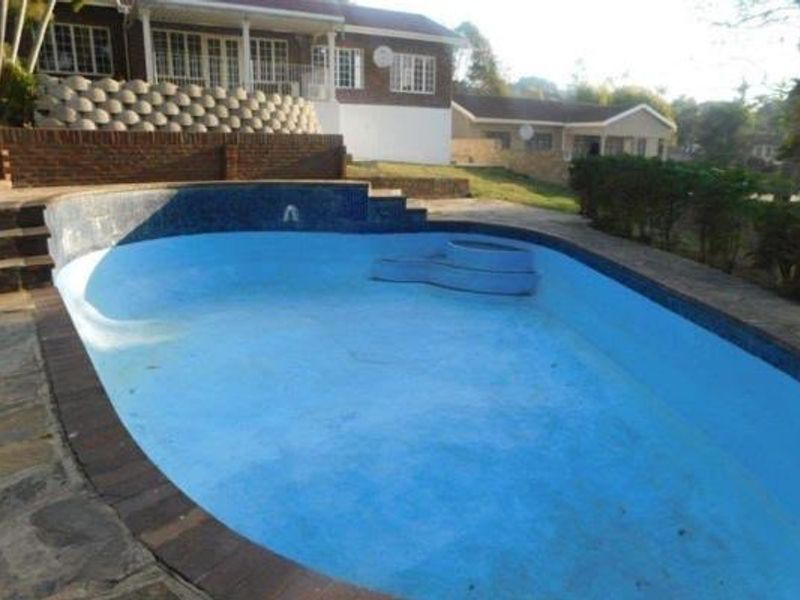 An outdoor swimming pool area featuring stone paving, a retaining wall, and a view of the rear house elevation.