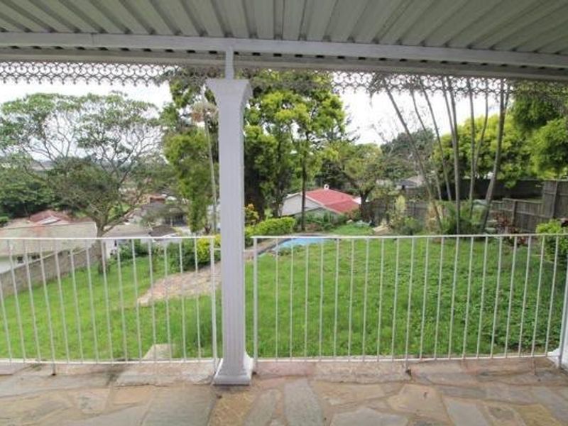 A covered patio featuring stone flooring and a metal balustrade, offering an elevated view over the rear garden and surrounding neighborhood.
